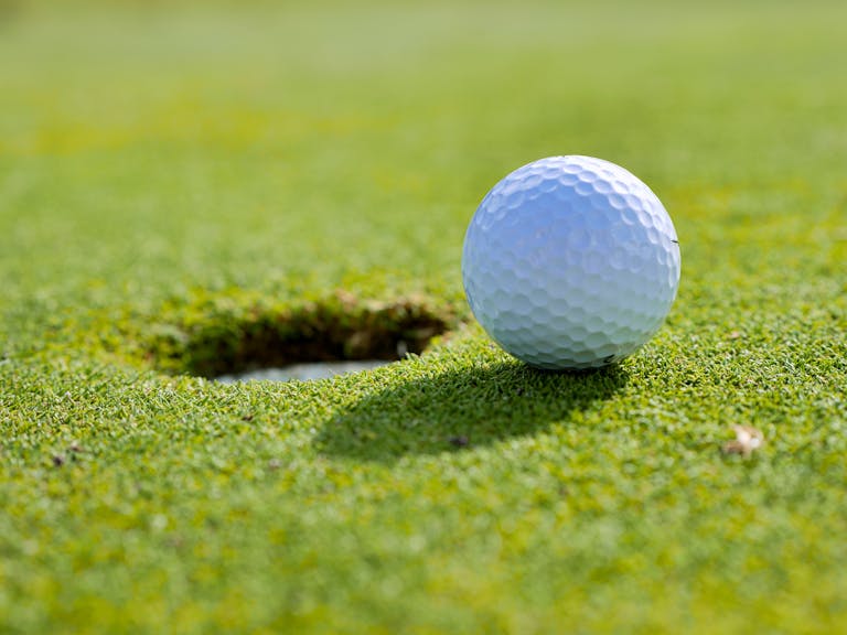 Close-up of a golf ball near the hole on a sunlit golf course green.
